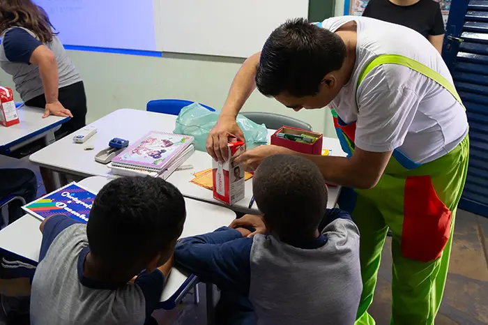 Educador interage com alunos em sala de aula, explicando conceitos de reciclagem e sustentabilidade no projeto Lixinho ou Lixão.