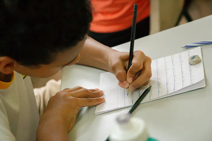 Jovem participante escreve à mão durante oficina do projeto Letra Jovem, que incentiva a leitura e a expressão criativa.